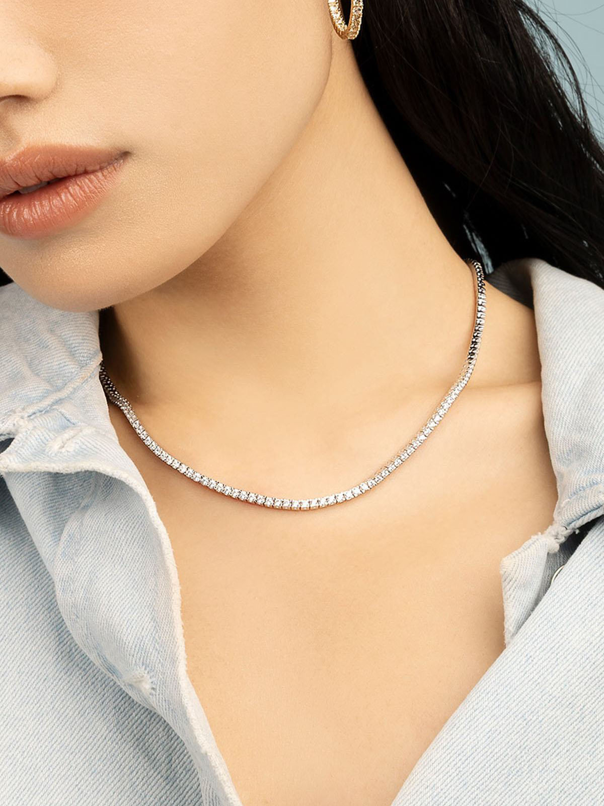Close-up of a person wearing a sterling silver pave necklace with white zirconia with a light blue shirt.