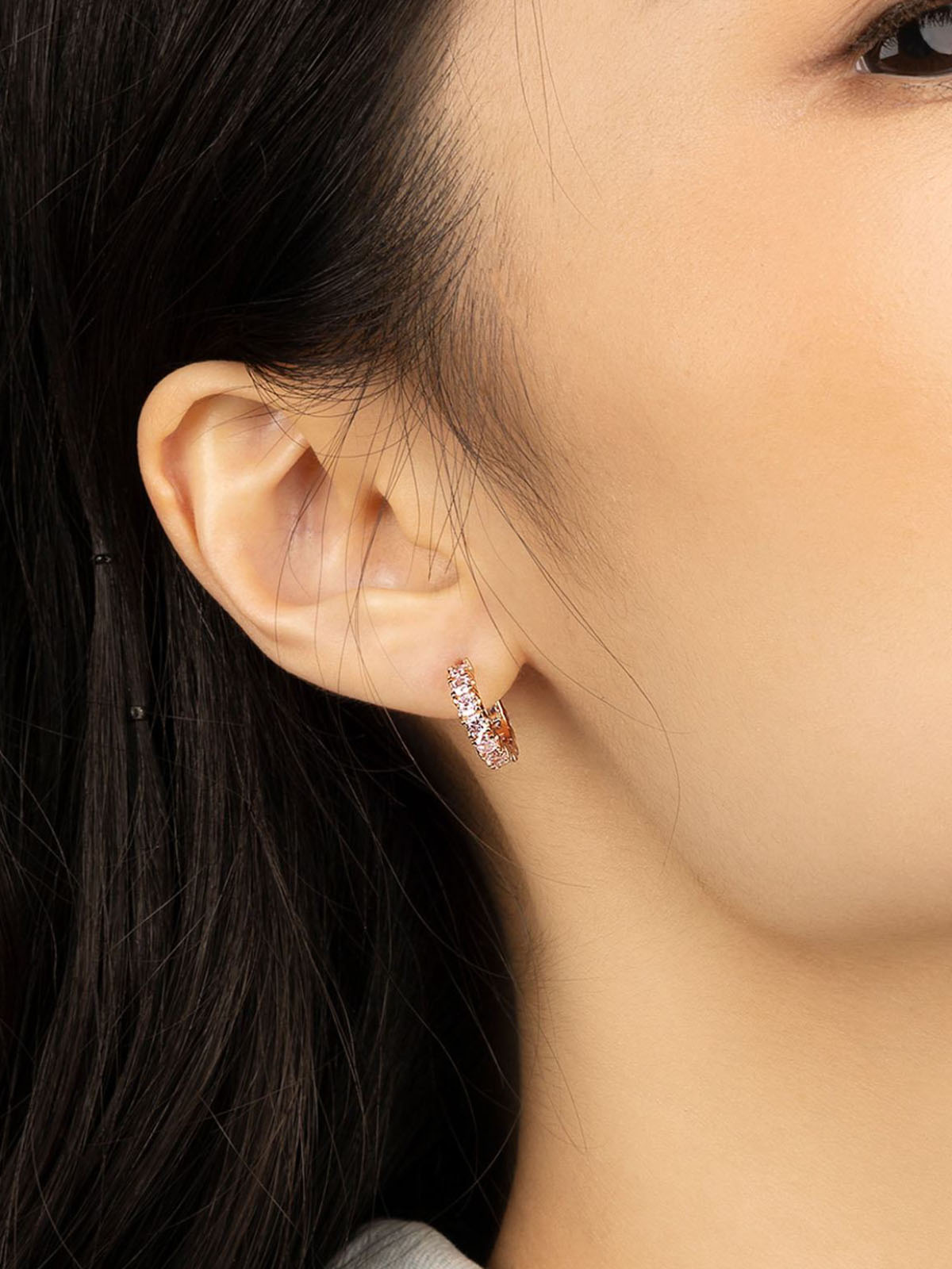 Close-up of an ear wearing a diamond earring with dark hair and skin background
