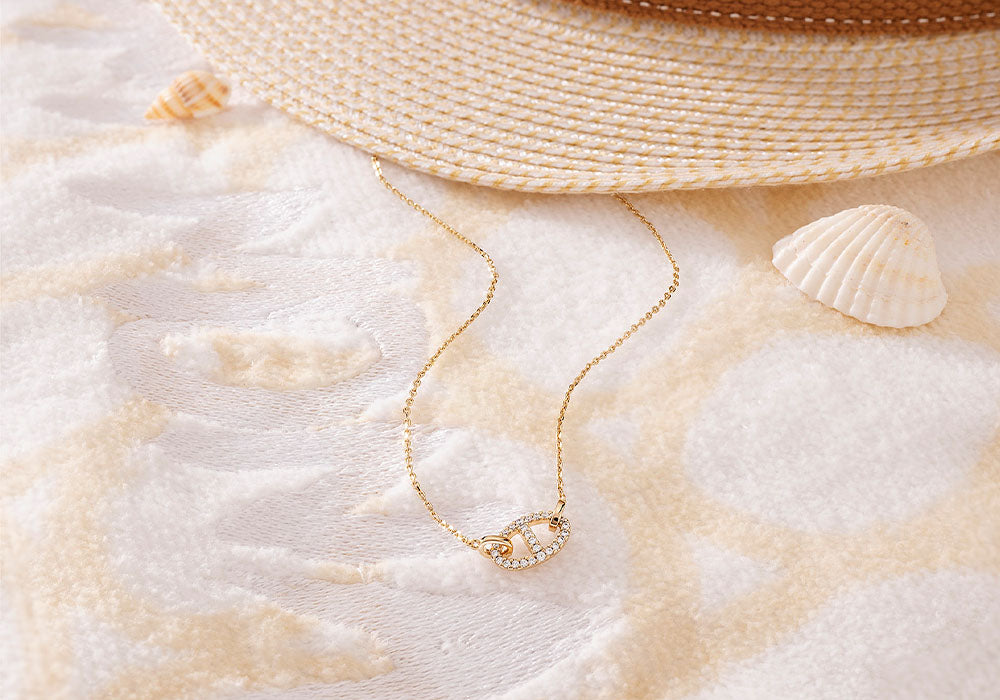 Gold-plated Maille Marine necklace with pavé details on a textured surface with shells