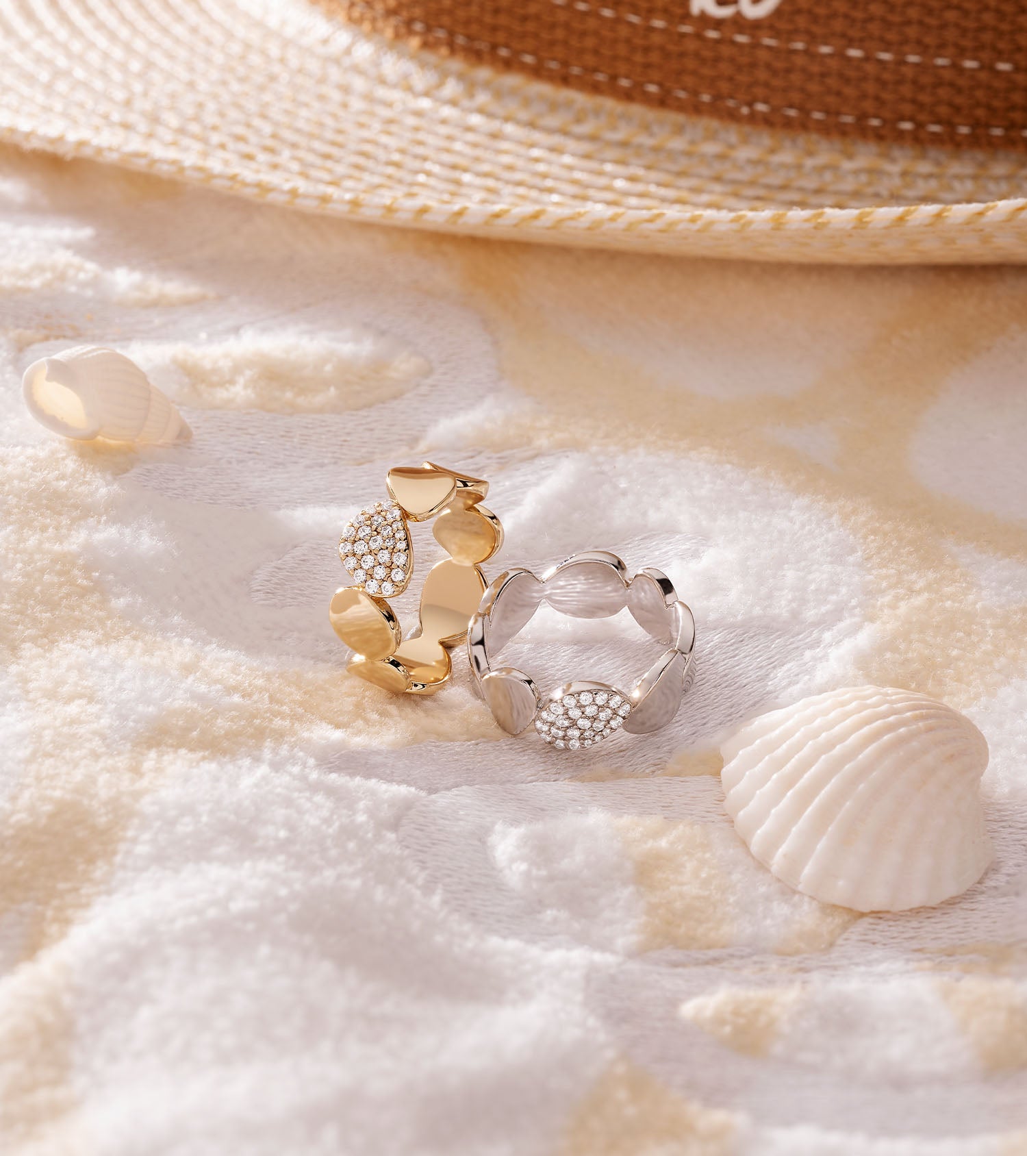 Two rings on sand with shells and a straw hat in the background