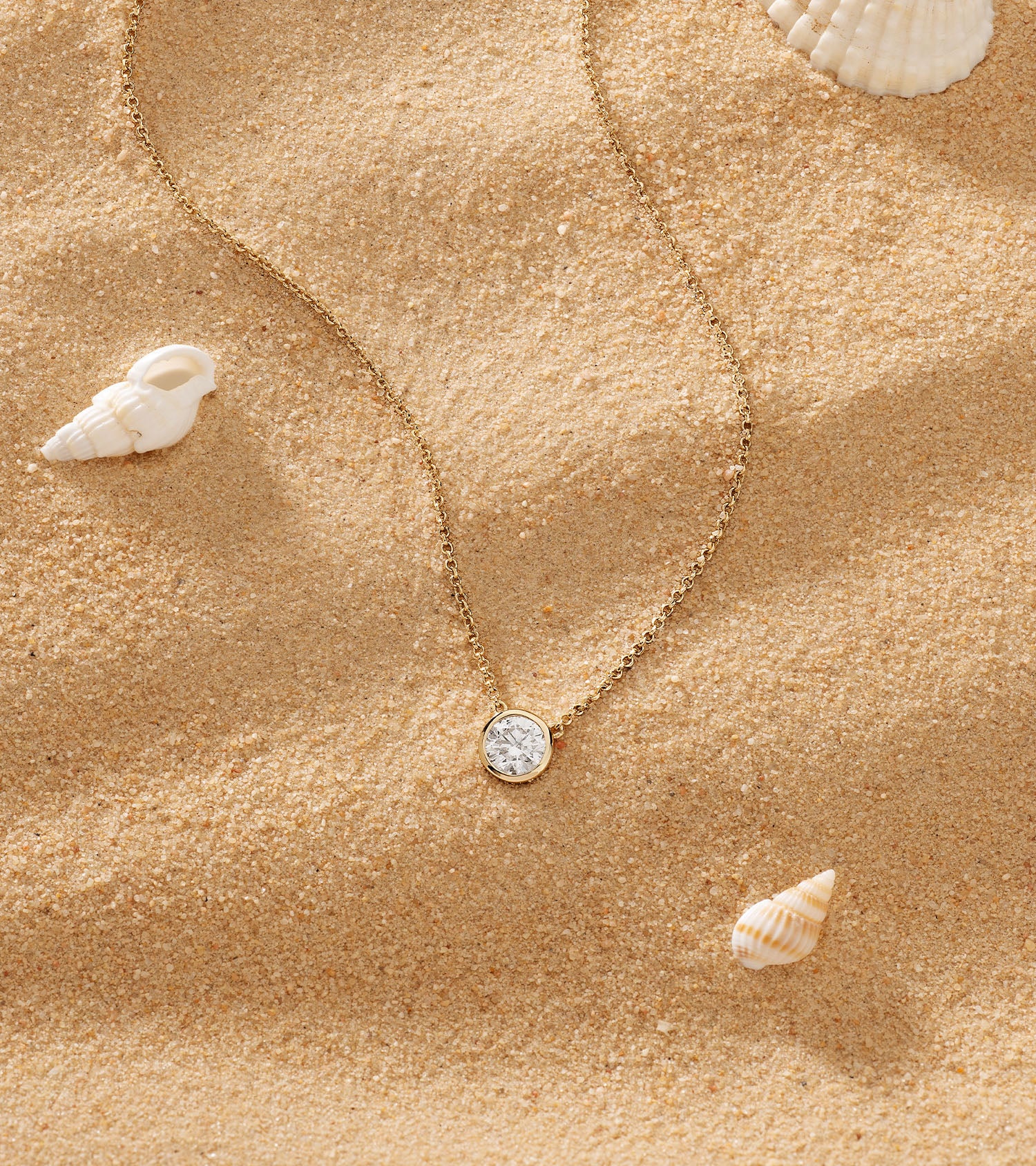 Gold necklace with a pendant on sand with shells