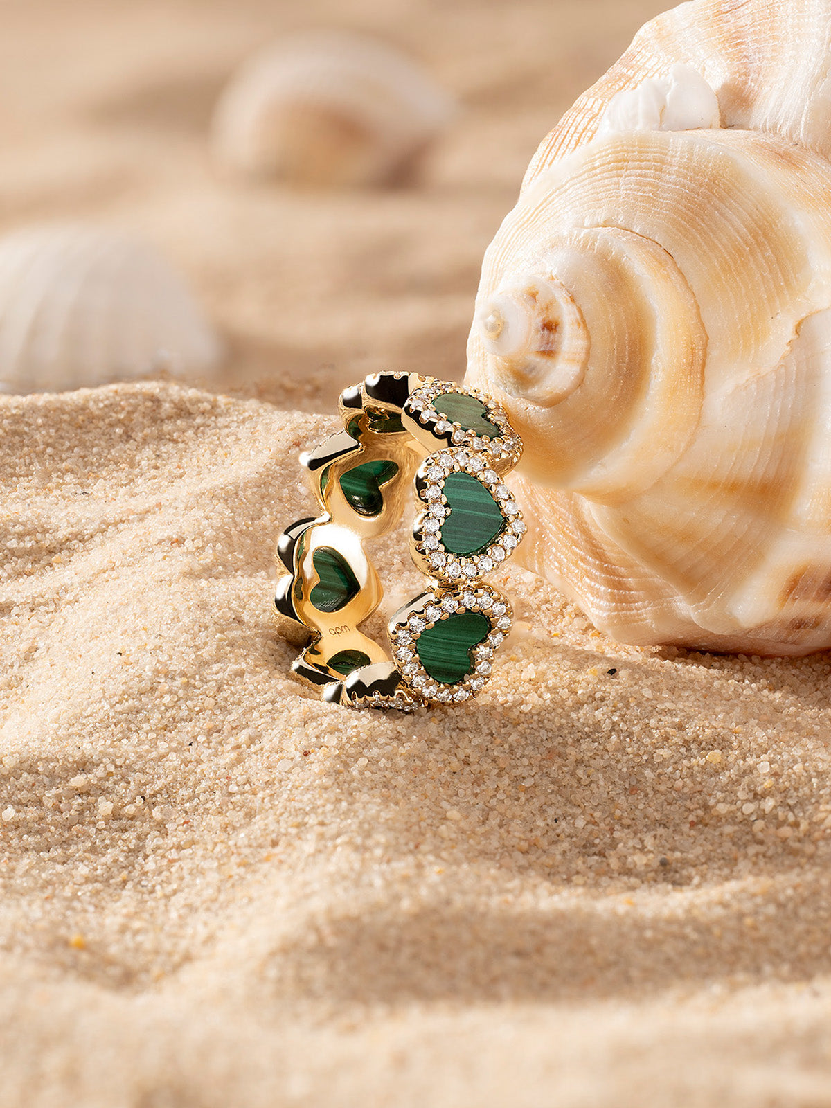 Gold-plated ring with heart-shaped Malachite and pavé details on sand with shells in the background 