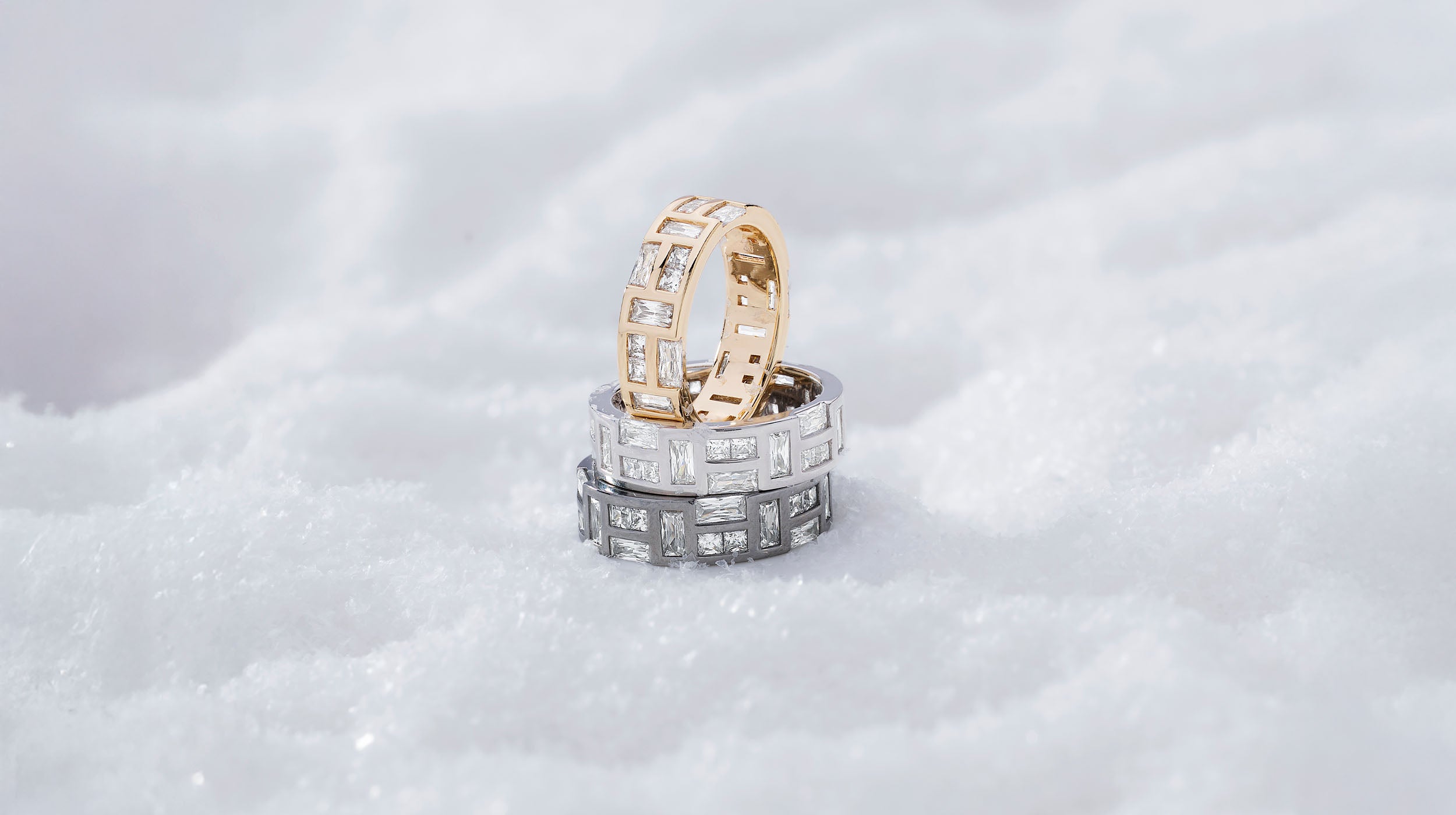 Three APM MONACO yellow gold, dark grey and silver rings stacked on a textured white surface