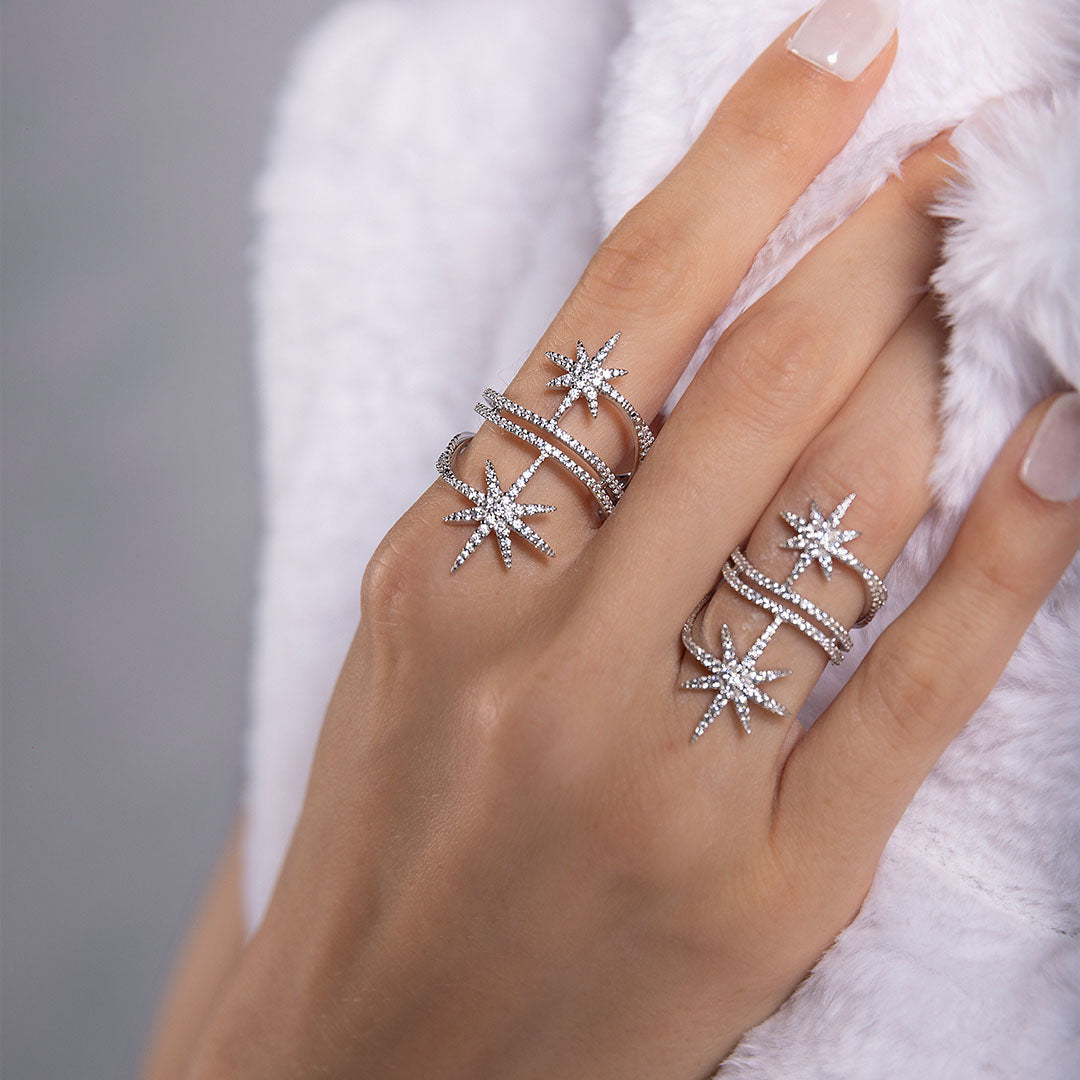 Hand wearing multiple silver star-shaped rings from APM MONACO on a neutral background