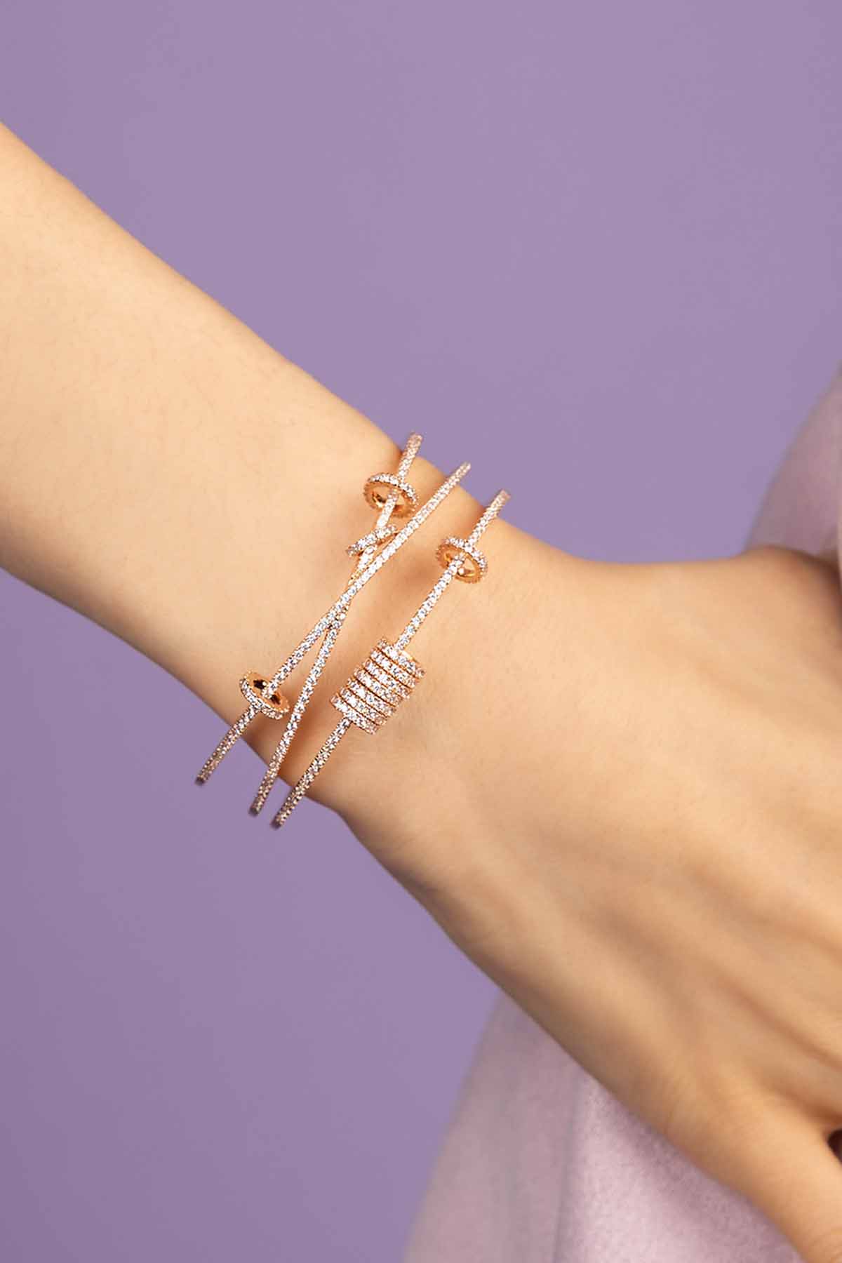 APM MONACO cuff with sliding rings design in rose gold on a wrist against a purple background