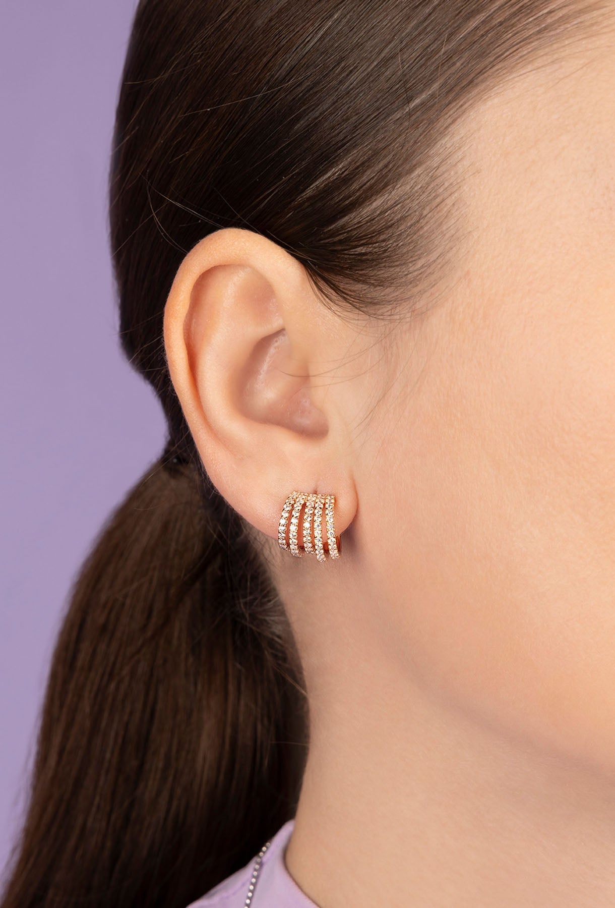 Close-up of a person wearing APM MONACO five hoops earrings in rose gold against a purple background