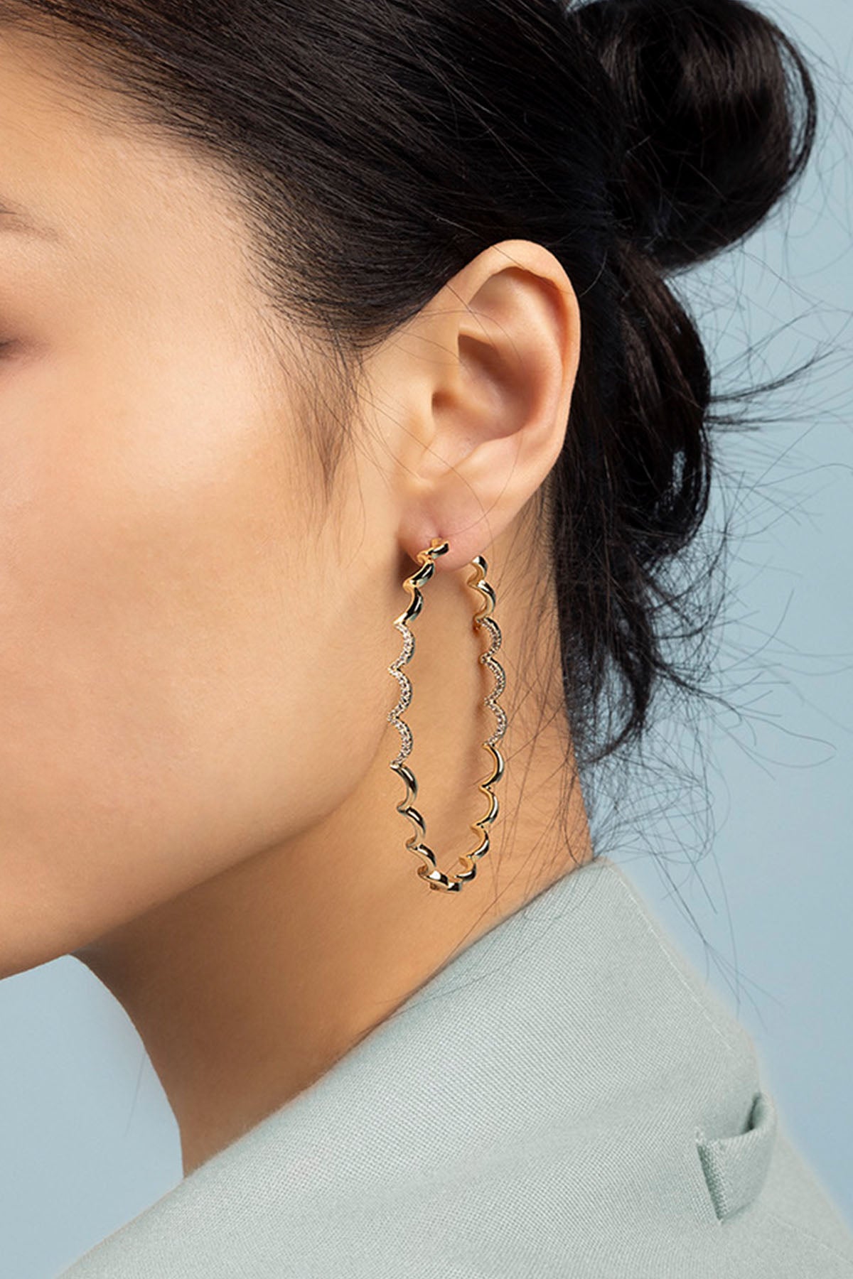 Close-up of a person wearing gold hoop earrings with a light blue background
